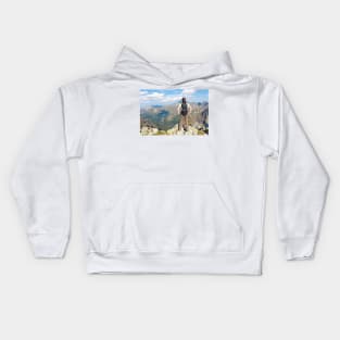 Woman with backpack standing on the edge, looking at mountains Kids Hoodie